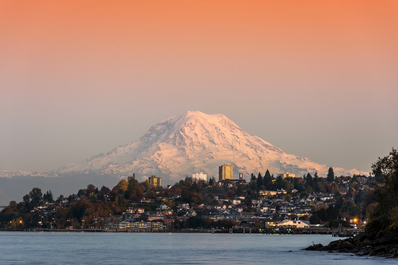 Tacoma, Washington Ruston Way Waterfront with Hillside of homes and buildings and Mount Tahoma (Rainier) in the background. Orange Sky and Hue to the sky