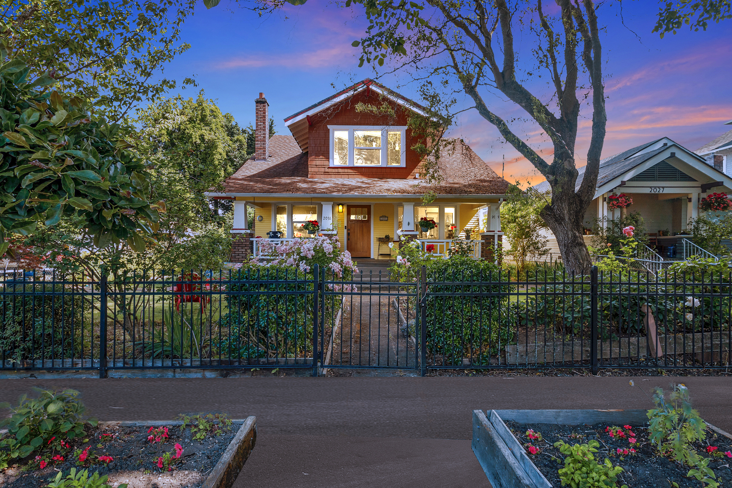 Yellow craftsman home listing glowing at twilight behind a landscaped front yard in Tacoma