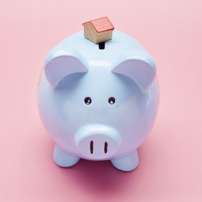 Still life of blue piggy bank and small house on pink background