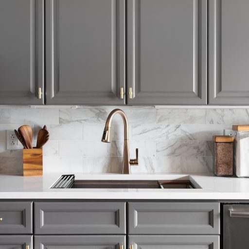A kitchen sink detail shot with grey cabinets, a white marble co